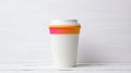 A white paper coffee cup with a yellow lid and a pink sleeve on a white wooden background. The cup is in the center of Royalty Free Stock Photo