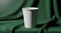 White paper cup centered on a green fabric backdrop. The cup is cylindrical and Royalty Free Stock Photo
