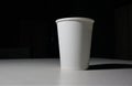 White paper cup with coffee in it sitting on a white table. using dim lights so that the shadows are clearly visible