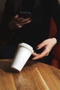 White paper cup takeaway mockup, on a table in a cafe. A woman& x27;s hand holds a cup and a smartphone. The concept of a Royalty Free Stock Photo