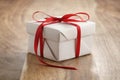 White paper gift box with thin red ribbon bow on old wood table Royalty Free Stock Photo