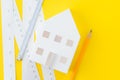 White paper house, yellow pencil and white measuring tapes with centimetre and inches on vivid yellow background, architecture, Royalty Free Stock Photo