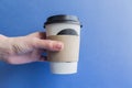 White paper kraft disposable cup for coffee with black plastic lid in a female hand. coffe to go on blue background Royalty Free Stock Photo