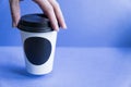 White paper kraft disposable cup for coffee with black plastic lid in a female hand. coffe to go on blue background Royalty Free Stock Photo