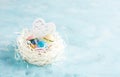 White paper nest with three vintage Easter eggs and wooden heart on blue background Royalty Free Stock Photo