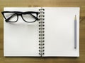 White paper note book with grey pencil and black glasses on wood