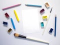 White paper notepad and painting art supplies. Colorful artistic flat lay on white background.