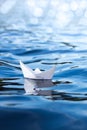 White paper ship on blue water, vertical frame, origami boat floats on the waves, concept of travel, holidays, symbol of freedom a Royalty Free Stock Photo