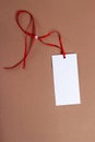 White paper tag with red ribbon and a bead on the brown background Royalty Free Stock Photo