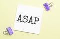 white paper with text asap on a yellow background with stationery Royalty Free Stock Photo