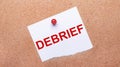 White paper with the text DEBRIEF is attached to the wooden background with a red button Royalty Free Stock Photo