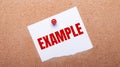 White paper with the text EXAMPLE is attached to the wooden background with a red button