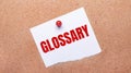 White paper with the text GLOSSARY is attached to the wooden background with a red button Royalty Free Stock Photo