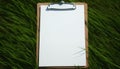 White paper on wooden clipboard on green grass background. Mockup