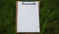 White paper on wooden clipboard on green grass background. Mockup