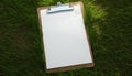 White paper on wooden clipboard on green grass background. Mockup