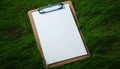 White paper on wooden clipboard on green grass background. Mockup