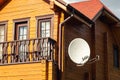 White parabolic satellite antena dish hanged on wall of modern wooden country house villa. Wireless television broadcasting