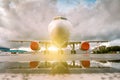 White passenger airplane parked near the hangars with reflection in a puddle at the setting evening sun. Front view Royalty Free Stock Photo