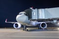 A white passenger jet plane at the air bridge connected to an external power supply on an airport night apron