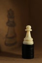 White pawn on wooden table in front of drawn queen chess piece Royalty Free Stock Photo