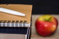 A white pen on a notebook and an apple on a table. Education concept.