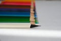 A white pencil with a black tip lies next to colored pencils folded in a row.