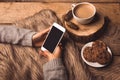 White phone in the hands of the girl, coffee cookies, cones and fur