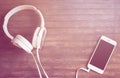 White phone and headphones flat lay on wooden table. Warm pink light toned photo.