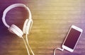 White phone and headphones on wooden table. Warm yellow light toned photo. Royalty Free Stock Photo