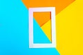 White photo frame on bright geometric orange, yellow and blue background. Minimal concept.
