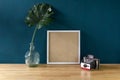 White photo frame on wood table decorated with tropical monstera leaf and vintage camera