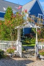 White picket fence with charming arbor covered with roses into yard of blue frame house with American and rainbow flags flying Royalty Free Stock Photo