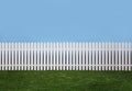 White picket fence with green grass and a blue sky background Royalty Free Stock Photo