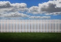 White picket fence with green grass and fluffy clouds in the background Royalty Free Stock Photo