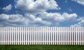 White picket fence with green grass and fluffy clouds in the background Royalty Free Stock Photo