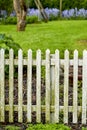 White picket fence and green grass in a home garden or park. Closeup of wooden gate post covered in moss in a lush Royalty Free Stock Photo