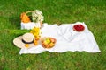 white picknick blanket on fresh grass with basket, fruits, flowers, straw hat