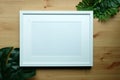 White picture frame and green monstera leaf on wooden background Royalty Free Stock Photo