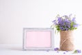 White picture frame with lovely purple flower in vase on white wooden table