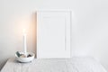 White picture frame mockup scene. Christmas seasonal still life. Burning candle in ceramic candle holder. Scandinavian