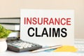 white piece of paper with the text insurance claims stands on the desk against the background of books, selective focus