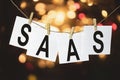 White pieces of paper with the text SaaS software as a service hang on a rope against a multicolored bokeh background Royalty Free Stock Photo