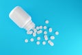 White pill tablets with white pill bottle over blue background, medical treatment, pharmaceutical or medication concept, flat lay