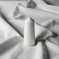 A white pillar candle is placed upright on a soft, white fabric backdrop Royalty Free Stock Photo