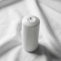 White pillar candle stands upright on a soft white fabric background Royalty Free Stock Photo