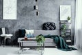 Pillow on black metal chair next to grey sofa with pillow in dark living room interior with maps on empty concrete wall Royalty Free Stock Photo