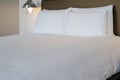 White pillows and bed in hotel room. Cozy white bed in the morning. White sheets and pillow on bed in modern hotel bedroom. Royalty Free Stock Photo