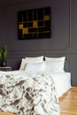 White pillows and blanket on a double bed in a grey bedroom interior with a black and golden painting. Real photo