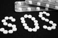 White pills on black background, which forming the word SOS, with a blister of pills on background.